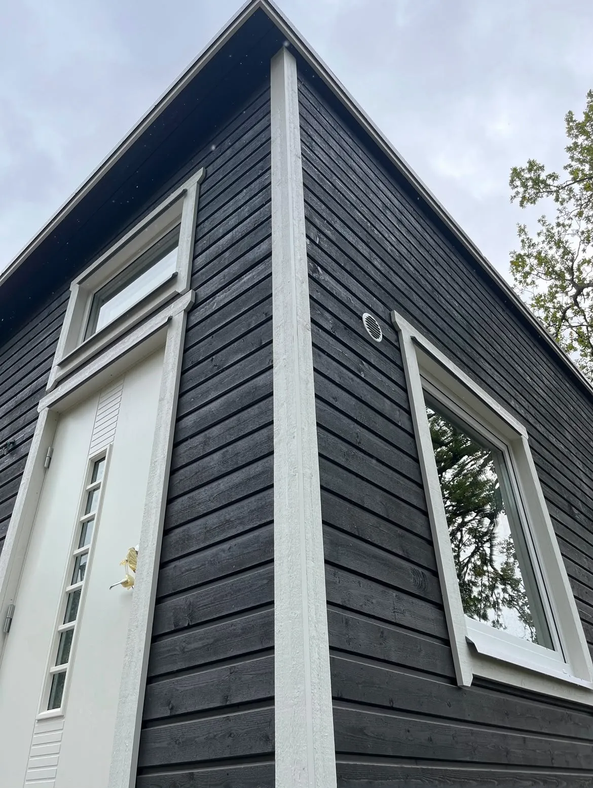 Mörk träfasad med vit ytterdörr och fönster